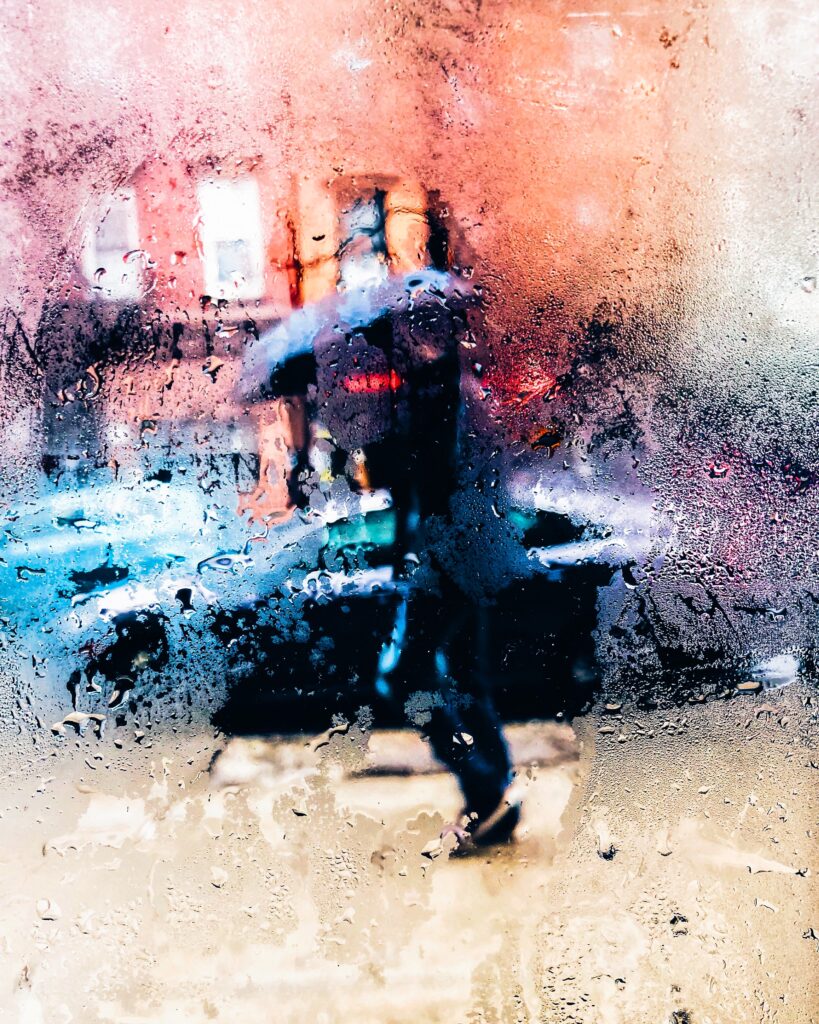Blurry image of person walking on city sidewalk with umbrella on rainy day
